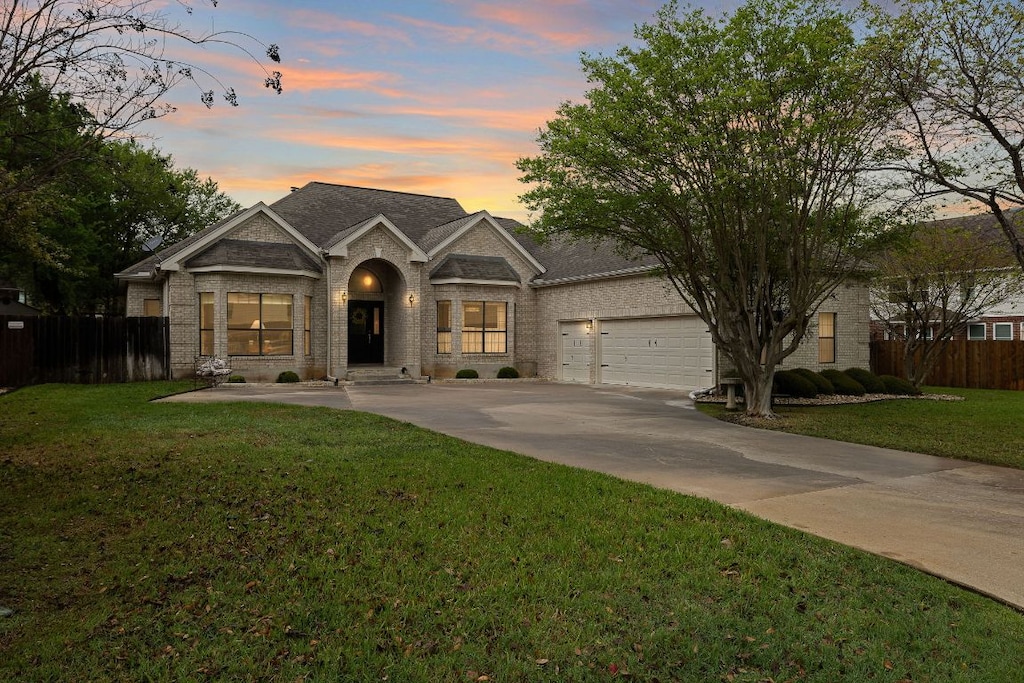 view of front of home featuring driveway, brick siding, fence, and a yard