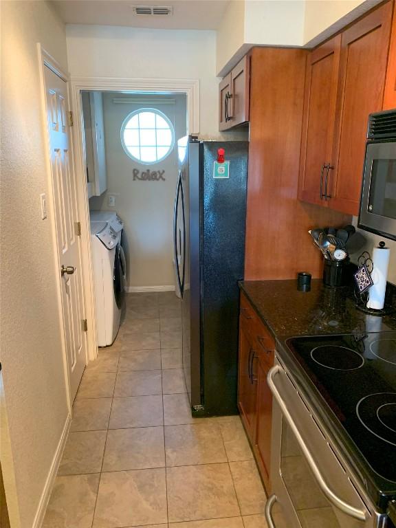 kitchen with light tile patterned flooring, visible vents, independent washer and dryer, brown cabinets, and black appliances