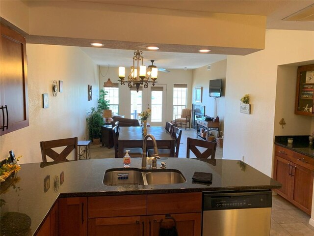 kitchen with dishwasher, brown cabinets, dark stone countertops, a sink, and open floor plan