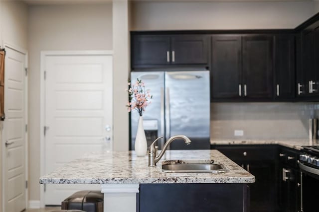 13800 Lyndhurst St Unit 325, Austin, TX 78717 - kitchen with appliances with stainless steel finishes, a sink, a center island with sink, light stone countertops, and dark cabinetry