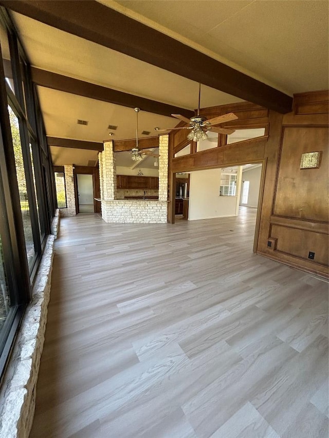 712 Rolling Green Dr, Lakeway, TX 78734 - unfurnished living room featuring wood walls, light wood-style floors, visible vents, vaulted ceiling with beams, and ceiling fan