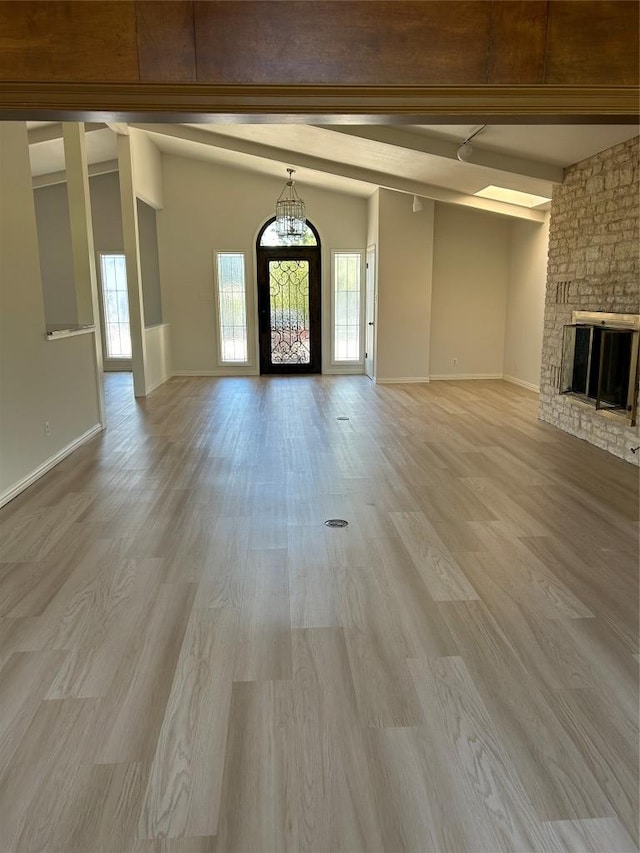 712 Rolling Green Dr, Lakeway, TX 78734 - unfurnished living room with a stone fireplace, vaulted ceiling with beams, light wood-style floors, and baseboards