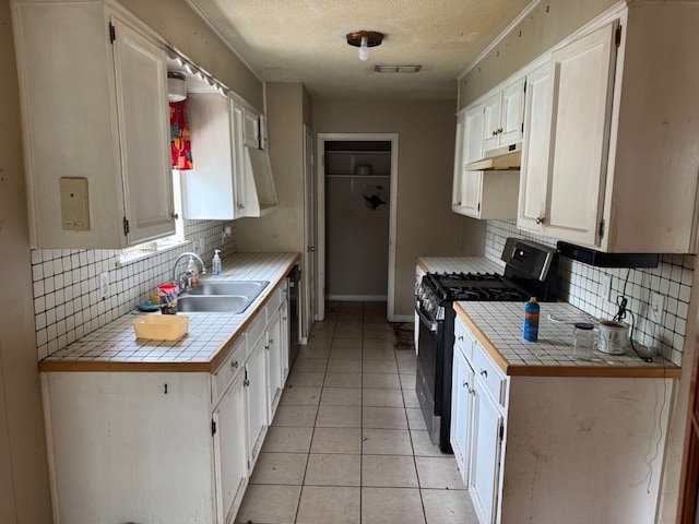 2100 Heights Blvd, Taylor, TX 76574 - kitchen with black gas stove, tile countertops, under cabinet range hood, tasteful backsplash, and a textured ceiling