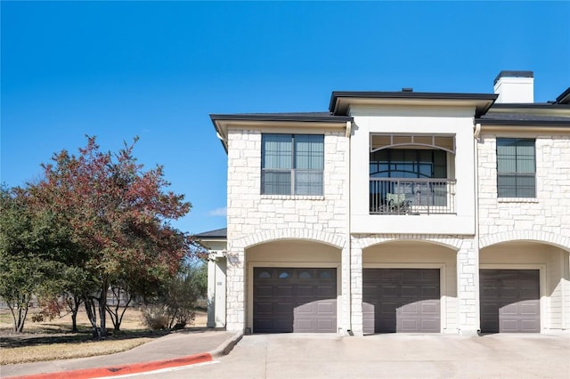 7701 Rialto Blvd Unit 617, Austin, TX 78735 - view of front of home featuring a garage, a balcony, stone siding, a chimney, and driveway