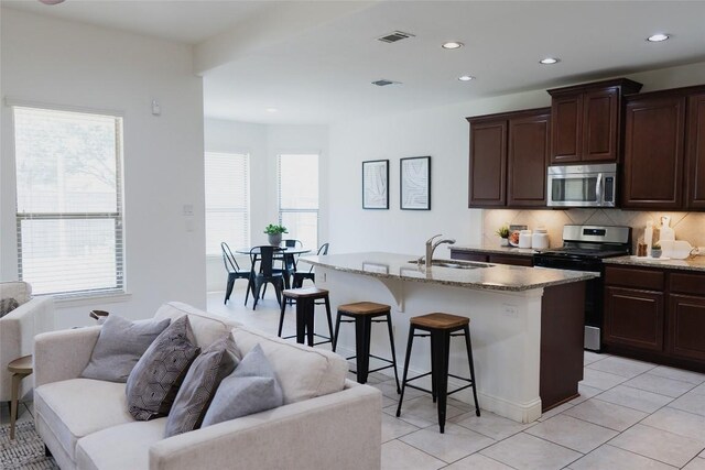 kitchen with a sink, backsplash, a kitchen bar, appliances with stainless steel finishes, and open floor plan