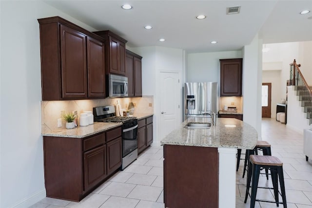 kitchen featuring a breakfast bar, a sink, visible vents, a kitchen island with sink, and appliances with stainless steel finishes