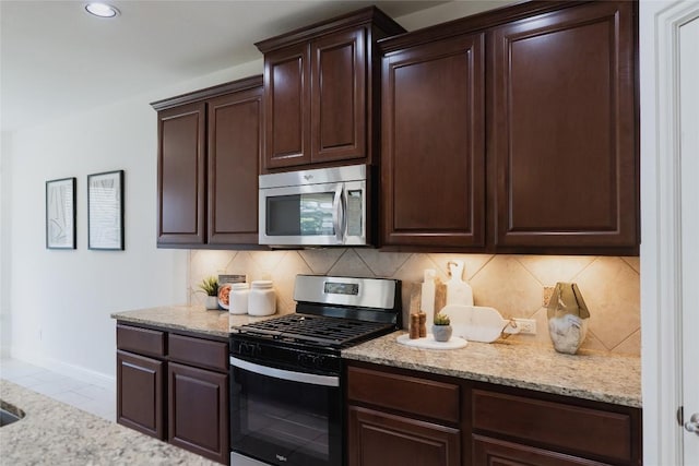 kitchen with baseboards, light stone countertops, stainless steel appliances, dark brown cabinets, and backsplash