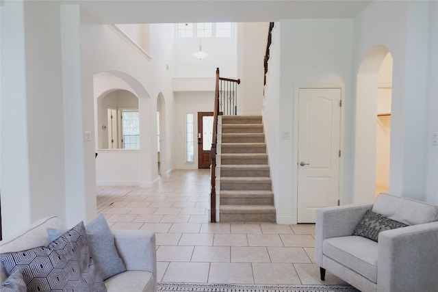 entryway featuring stairway, light tile patterned floors, baseboards, a high ceiling, and arched walkways