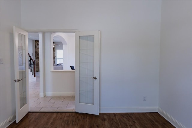 spare room with french doors, arched walkways, dark wood-type flooring, and baseboards