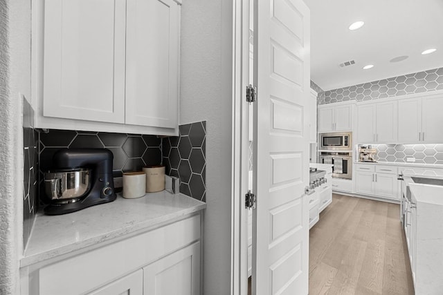 kitchen featuring white cabinets, stainless steel appliances, visible vents, and backsplash