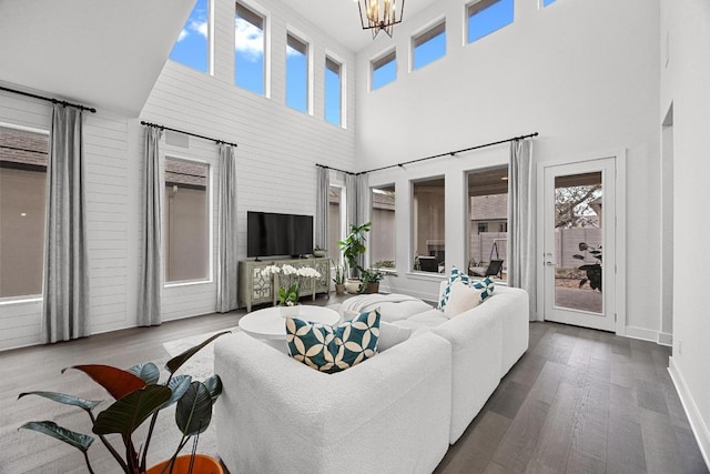 living room with a towering ceiling, a notable chandelier, wood finished floors, and baseboards