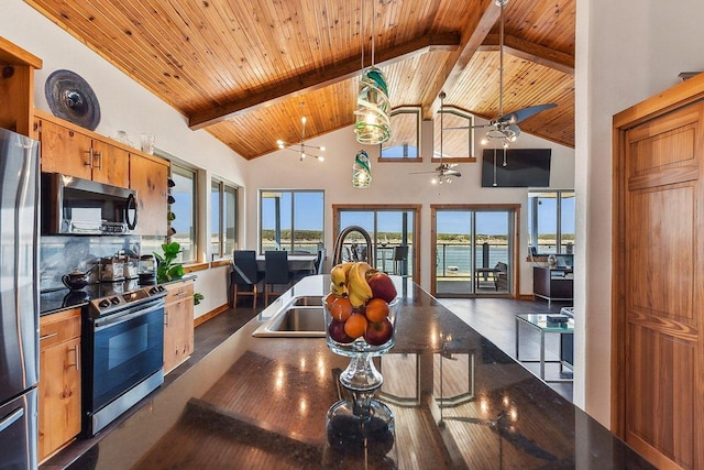kitchen with beamed ceiling, plenty of natural light, stainless steel appliances, dark countertops, and a sink