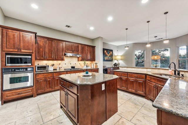 22000 Briarcliff Dr, Spicewood, TX 78669 - kitchen featuring appliances with stainless steel finishes, a spacious island, under cabinet range hood, decorative backsplash, and stone tile floors
