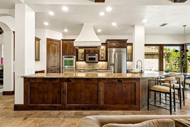 11 Hightrail Way, Austin, TX 78738 - kitchen with stainless steel appliances, backsplash, light stone counters, arched walkways, and a kitchen breakfast bar