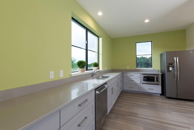 kitchen with light countertops, light wood finished floors, recessed lighting, appliances with stainless steel finishes, and a sink