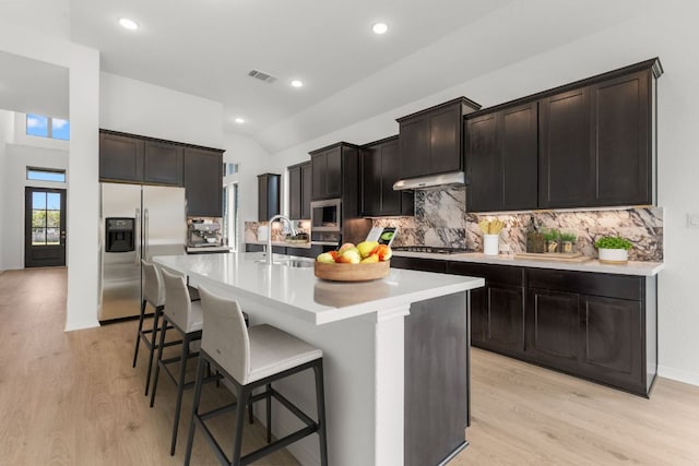 1800 Sauterne Dr, Leander, TX 78641 - kitchen featuring appliances with stainless steel finishes, decorative backsplash, light wood-style floors, a center island with sink, and a kitchen bar