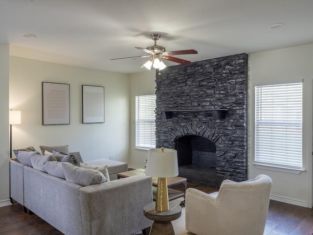 living area featuring baseboards, dark wood-style flooring, ceiling fan, and a stone fireplace