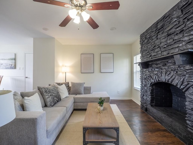 living room with baseboards, wood finished floors, a ceiling fan, and a stone fireplace
