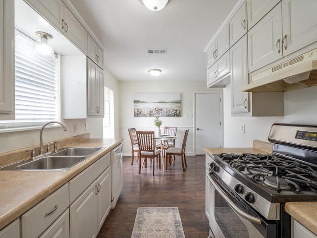 kitchen with light countertops, a sink, stainless steel gas range oven, under cabinet range hood, and visible vents