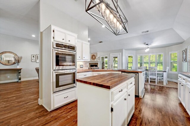 kitchen with a kitchen island, white cabinets, appliances with stainless steel finishes, a peninsula, and wood counters