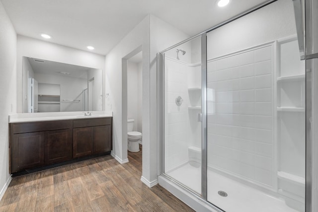 bathroom with toilet, vanity, a shower stall, wood finished floors, and recessed lighting