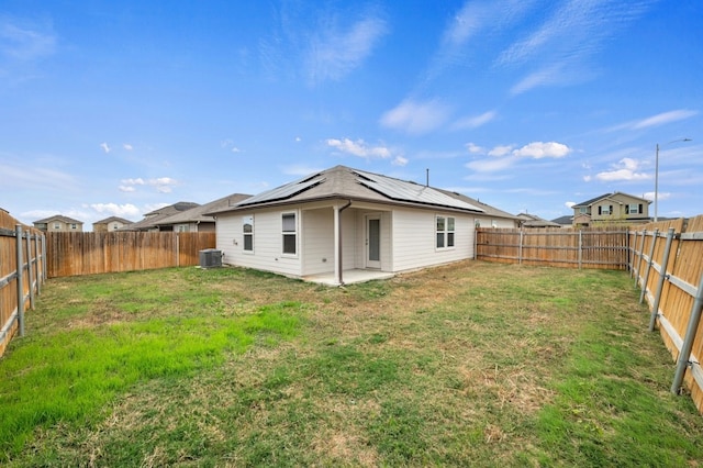 rear view of house featuring central air condition unit, a fenced backyard, roof mounted solar panels, a patio, and a yard