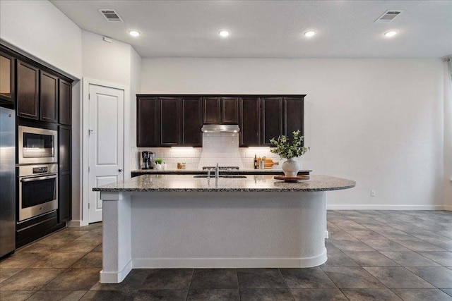 6725 Verona Pl, Round Rock, TX 78665 - kitchen with appliances with stainless steel finishes, under cabinet range hood, dark stone counters, backsplash, and an island with sink