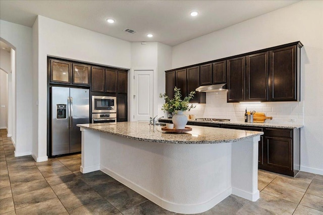 6725 Verona Pl, Round Rock, TX 78665 - kitchen with stainless steel appliances, arched walkways, light stone counters, decorative backsplash, and under cabinet range hood