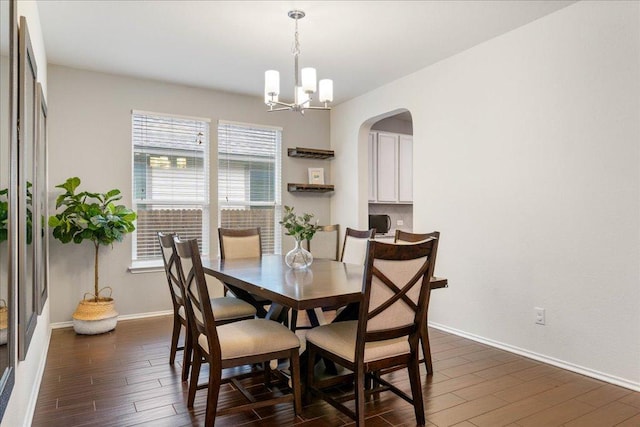 dining space featuring dark wood-type flooring, baseboards, a notable chandelier, and arched walkways