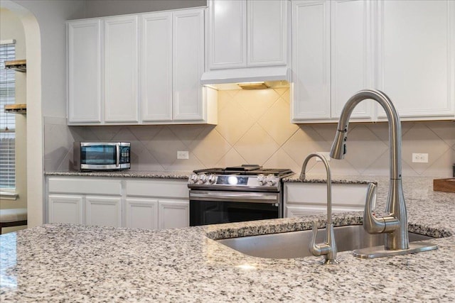 kitchen featuring white cabinetry, decorative backsplash, a sink, appliances with stainless steel finishes, and under cabinet range hood