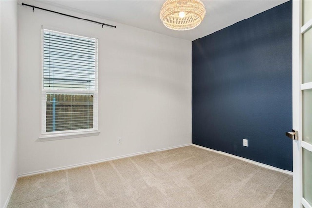 carpeted spare room featuring a chandelier and baseboards