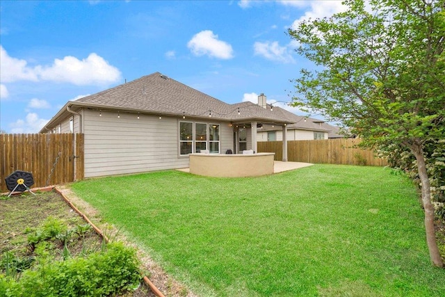 rear view of house featuring a chimney, a patio area, roof with shingles, a yard, and a fenced backyard