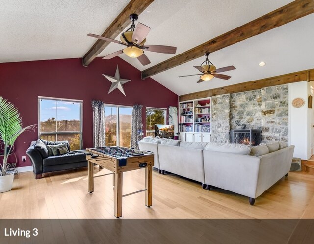 living room with lofted ceiling with beams, a textured ceiling, a fireplace, ceiling fan, and light wood-type flooring