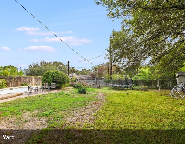 view of yard with a trampoline, a fenced backyard, and a patio