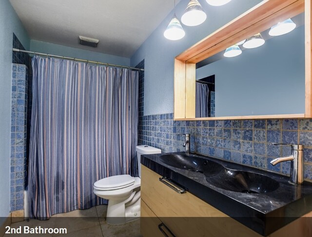 bathroom with toilet, vanity, tile patterned flooring, visible vents, and tile walls