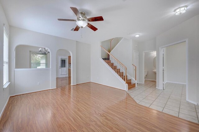 1012 Peyton Pl, Cedar Park, TX 78613 - unfurnished living room with arched walkways, stairway, a ceiling fan, a chandelier, and light wood finished floors