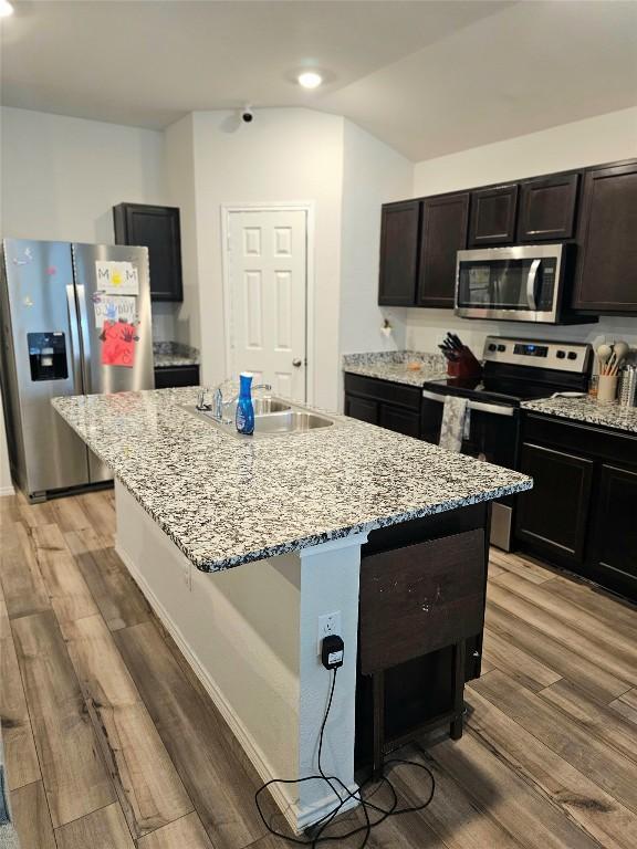 1124 Velvet Ct, Troy, TX 76579 - kitchen with stainless steel appliances, light stone counters, light wood finished floors, a center island with sink, and vaulted ceiling