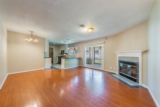 2004 Teakwood Dr, Austin, TX 78757 - unfurnished living room with wood finished floors, a tile fireplace, a chandelier, and a textured ceiling