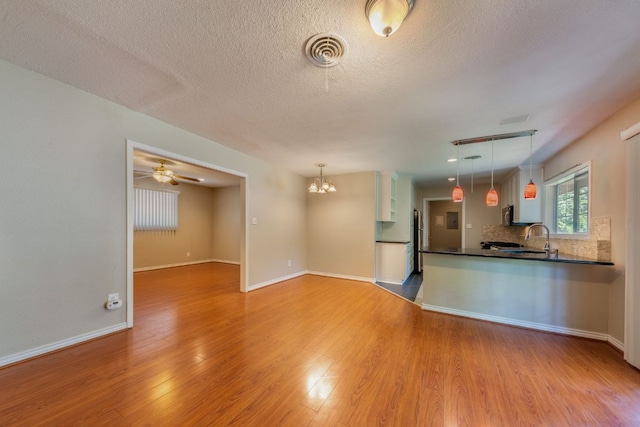 2004 Teakwood Dr, Austin, TX 78757 - kitchen featuring dark countertops, light wood finished floors, tasteful backsplash, decorative light fixtures, and a textured ceiling
