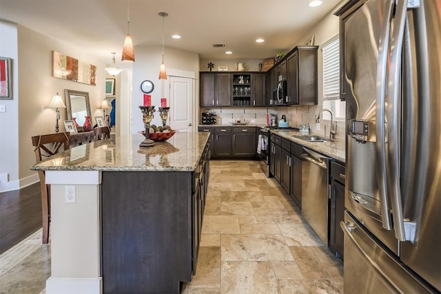 11913 Natures Bnd, Austin, TX 78753 - kitchen featuring appliances with stainless steel finishes, dark brown cabinets, stone tile flooring, a kitchen island, and light stone counters