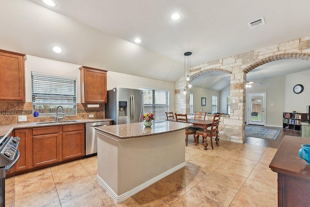 1411 Rowan Dr, Georgetown, TX 78628 - kitchen with appliances with stainless steel finishes, brown cabinets, healthy amount of natural light, a kitchen island, and vaulted ceiling
