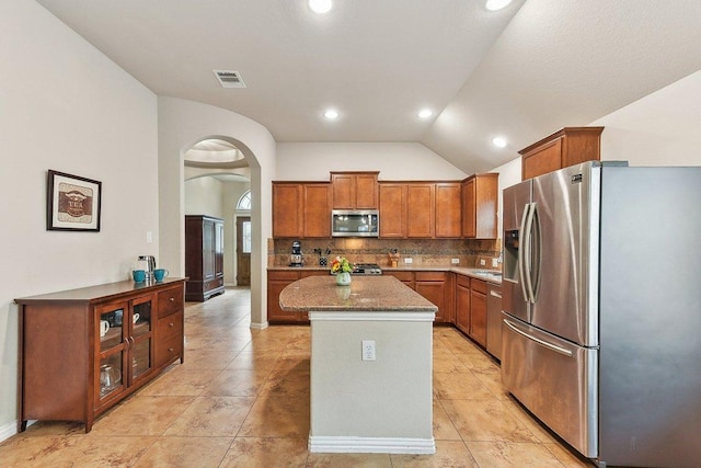 1411 Rowan Dr, Georgetown, TX 78628 - kitchen with appliances with stainless steel finishes, lofted ceiling, arched walkways, a kitchen island, and brown cabinets