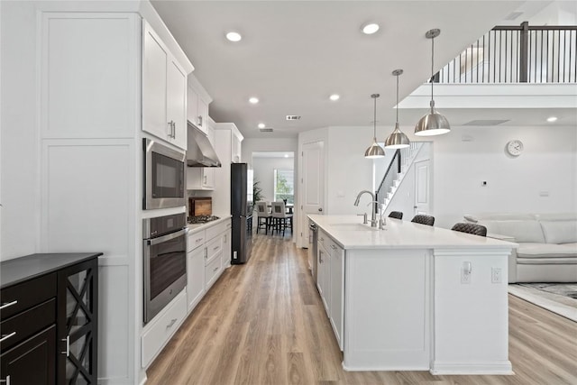 708 Leeward Pass, Leander, TX 78641 - kitchen with stainless steel appliances, under cabinet range hood, light wood finished floors, white cabinets, and light countertops