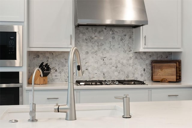 708 Leeward Pass, Leander, TX 78641 - kitchen featuring wall chimney range hood, stainless steel appliances, white cabinetry, light countertops, and backsplash
