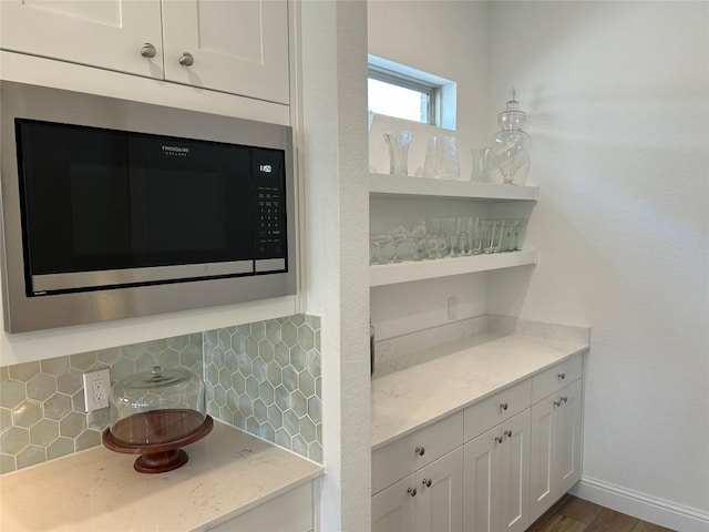 22046 Gateway Arch Dr, Porter, TX 77365 - detailed view of built in microwave, decorative backsplash, white cabinetry, open shelves, and light stone counters