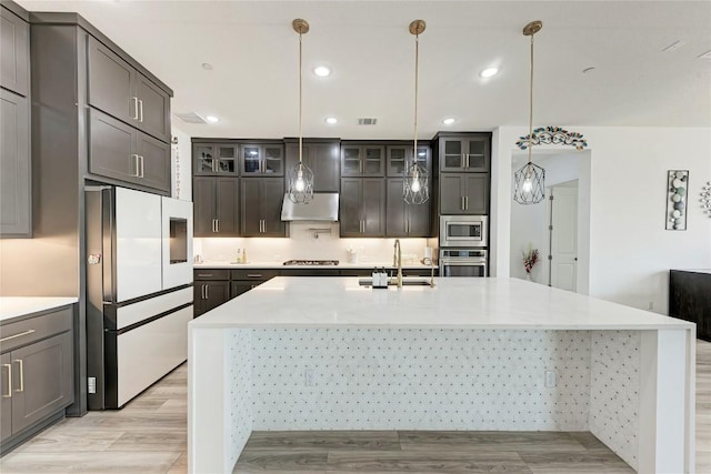 2420 Novara Trl, Leander, TX 78641 - kitchen with appliances with stainless steel finishes, under cabinet range hood, a spacious island, glass insert cabinets, and recessed lighting