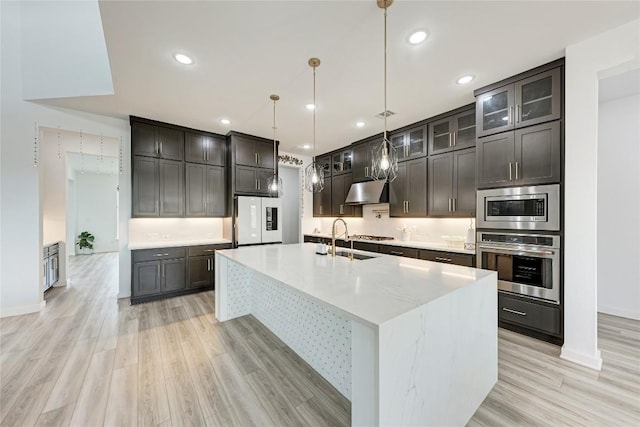 2420 Novara Trl, Leander, TX 78641 - kitchen featuring stainless steel appliances, light wood-type flooring, a large island, under cabinet range hood, and hanging light fixtures
