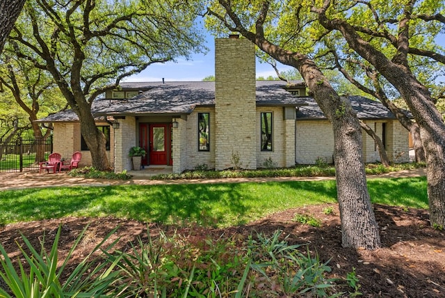 mid-century inspired home featuring brick siding, a front lawn, fence, and a chimney