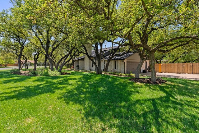 view of front facade featuring driveway, a front lawn, brick siding, a garage, and fence