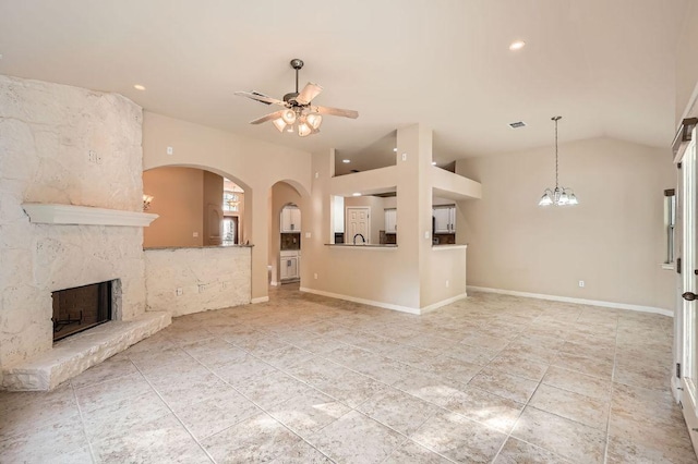 unfurnished living room with baseboards, a fireplace, arched walkways, ceiling fan with notable chandelier, and vaulted ceiling
